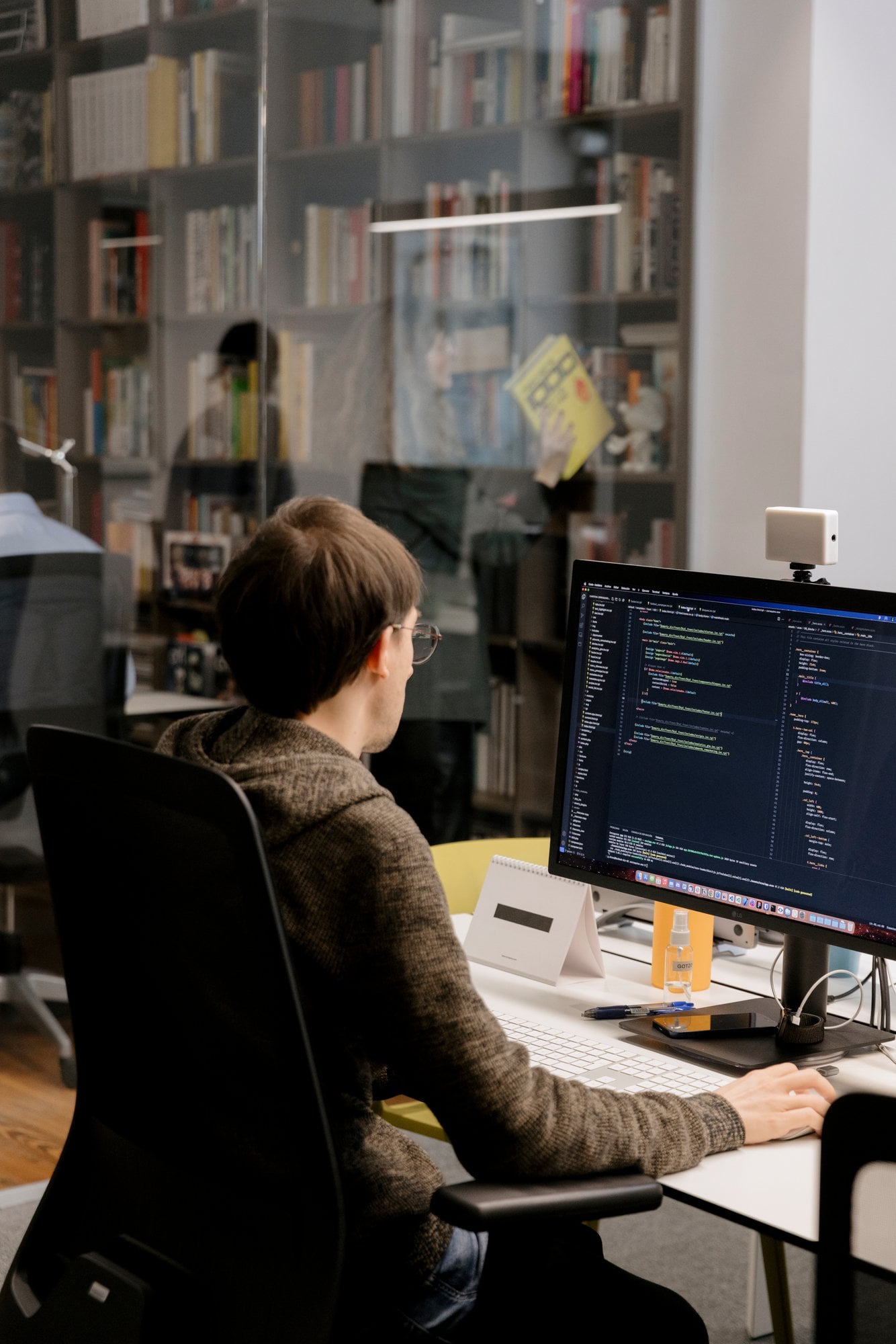 Desarrollador programando ante un monitor, con una librería al fondo