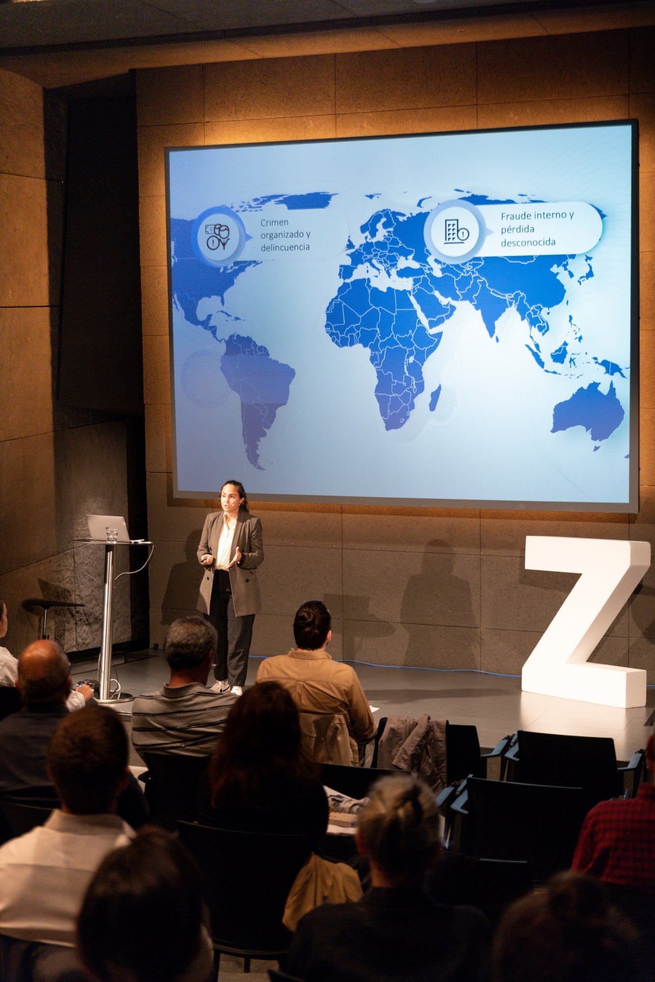 Speaker in front of a projected world map, next to a large Z, facing the audience