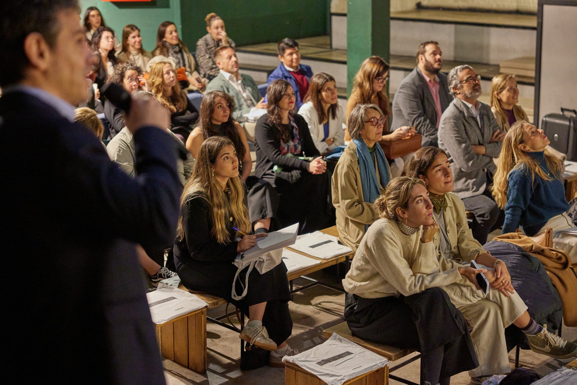 Público atento en gradas escuchando a un ponente con micrófono